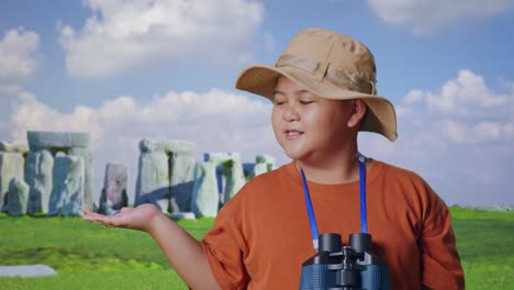 asian boy with a hat and binoculars smiling and pointing to side while traveling in stonehenge. boy researcher examines something, travel tourism adventure concept, close up