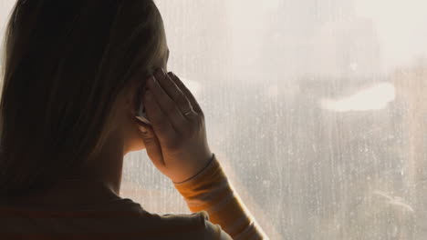 una mujer hablando por teléfono junto a la ventana.