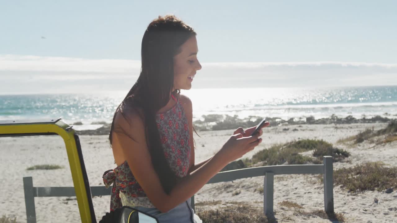 mujer caucásica feliz sentada en un buggy de playa junto al mar hablando en un teléfono inteligente