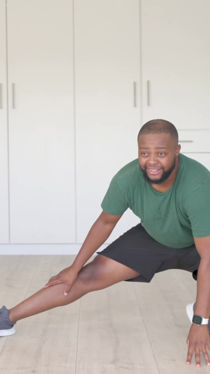 Vertical video: Starting set, man in green shirt doing side lunges at home with cabinets and watch