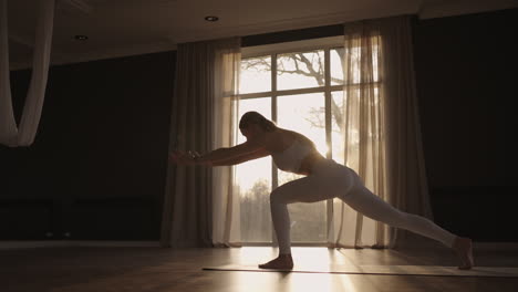 Slow-motion:-Young-woman-is-doing-yoga-in-a-white-room-filled-with-light-the-girl-performs-yoga-stands-and-elements-near-the-large-window.