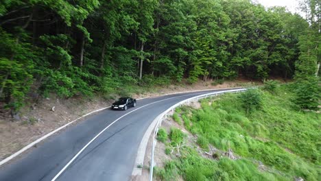 aerial view of a car passing by on a curly road at a forest between green trees