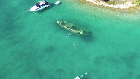 tourists swim at blue sea over shipwreck, ribolovac in solta island, croatia. - aerial
