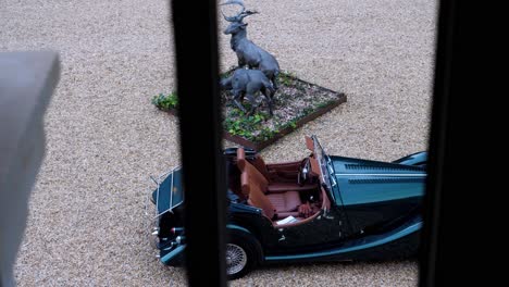 seen from the window, a green morgan classic car, parked on a gravel parking lot