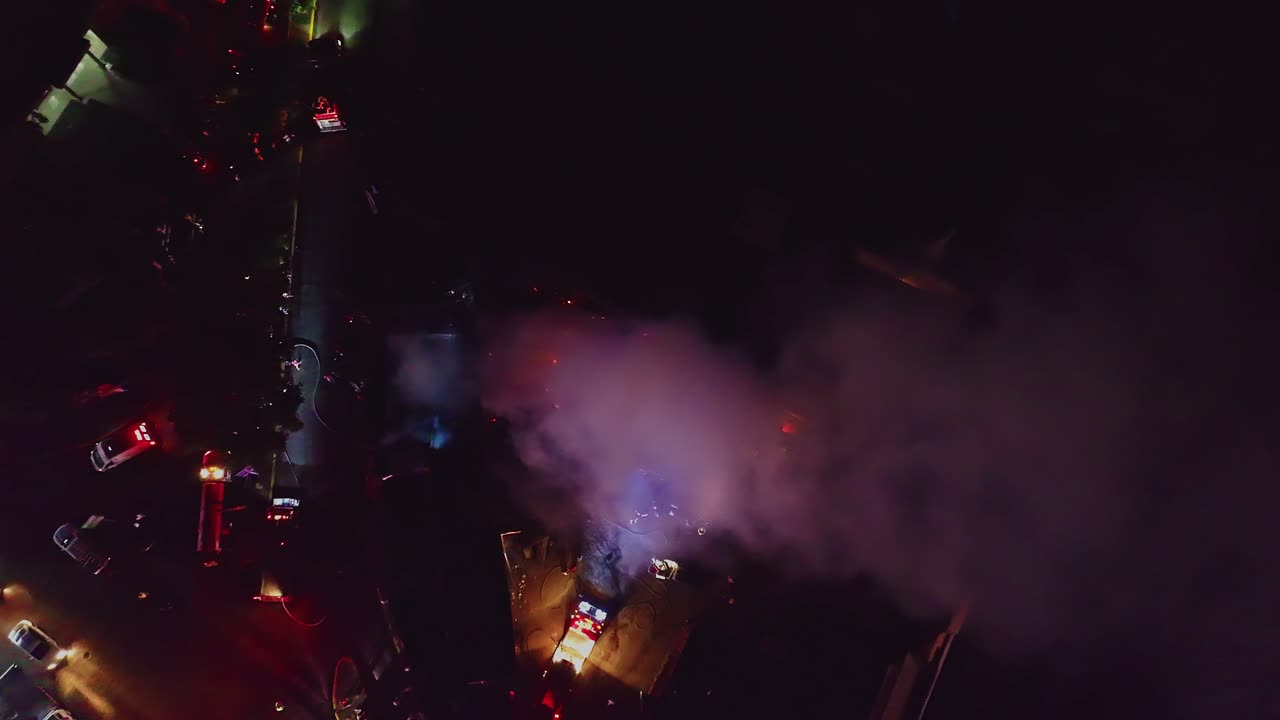Emergency response to a structure fire. Smoke rises as fire trucks and police cars surround scene at night, Dominican Republic. Aerial top-down ascending, copy space