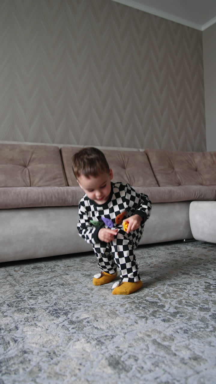 Dark-haired toddler boy picks up the details of his toys from the floor. Kid puts the toys into the sofa drawer. Low angle view. Vertical video.