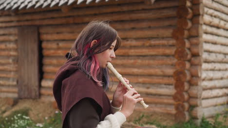 Teenage-girl-plays-folk-flute-standing-near-wooden-wall