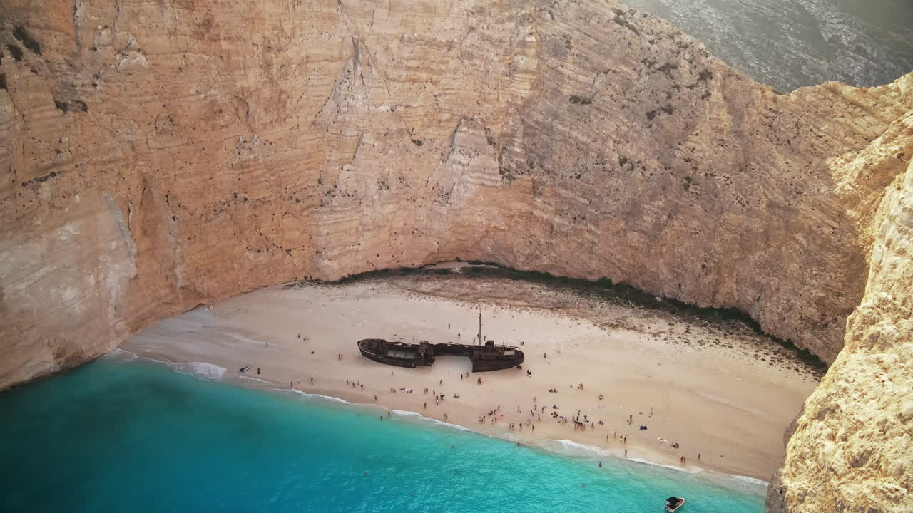 Aerial drone view of the Navagio beach on the Ionian Sea coast of Zakynthos, Greece. Rocky cliffs, resting people, blue water
