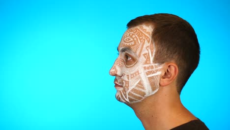 portrait of a handsome man with white paint on his face on a blue background. man looking sideways