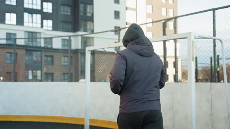 athlete jogging in outdoor sports arena with background featuring goalpost and urban high-rise buildings, emphasizing active lifestyle, determination, and fitness in a modern urban environment