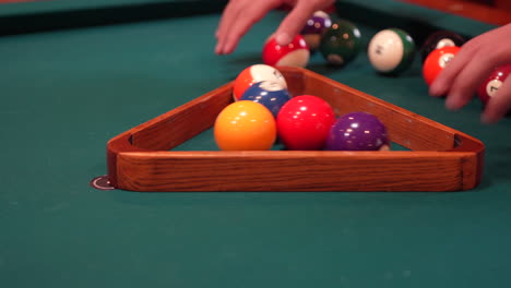 person racks 8 ball pool triangle closeup on the spot gathering solid and stripped billiard balls on table with green felt or cloth and tightening rack with hands before lifting wooden triangle