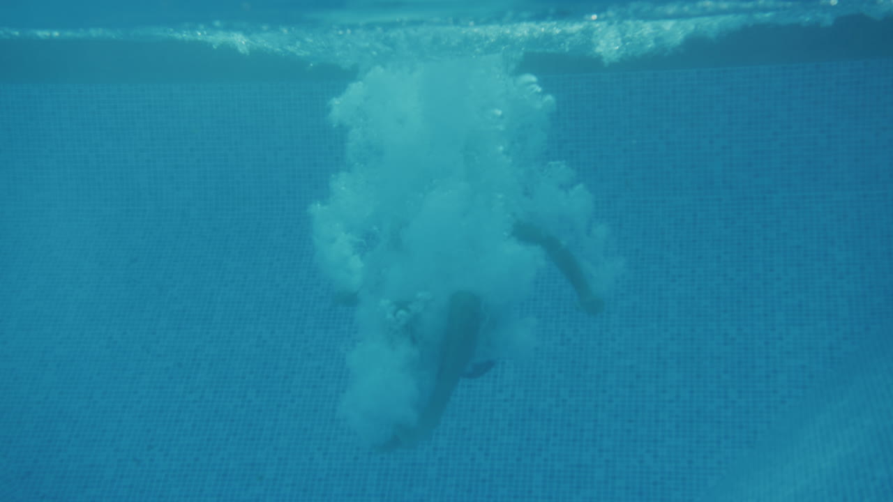 fotografía submarina de un padre saltando a la piscina observada por una madre y su hijo en vacaciones de verano en familia