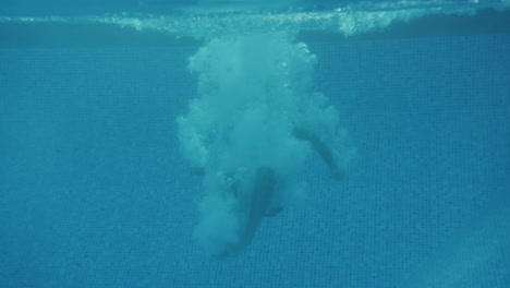 underwater shot of father jumping into swimming pool watched by mother and son on family summer vacation