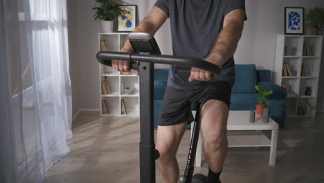 adult man is using stationary bike in home middle-aged person is caring about health keeping fit at self-isolation time