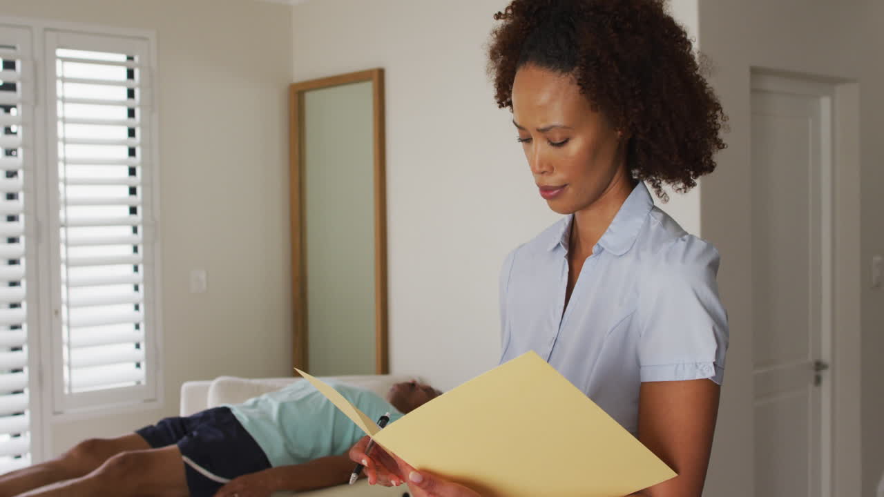 Portrait of mixed race female physiotherapist holding notebook and writing looking at camera