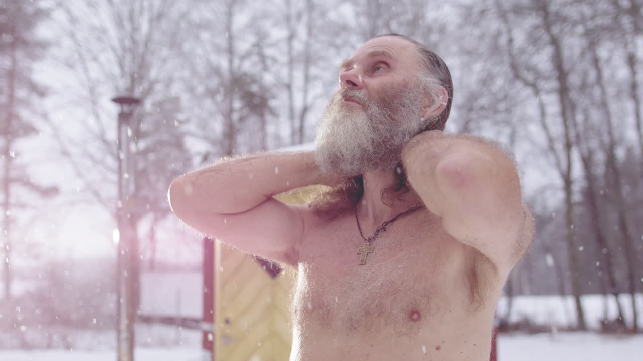 Scraggy man in falling snow loses himself in skyward meditation after sauna