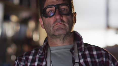 caucasian male knife maker in workshop putting on glasses and looking at camera