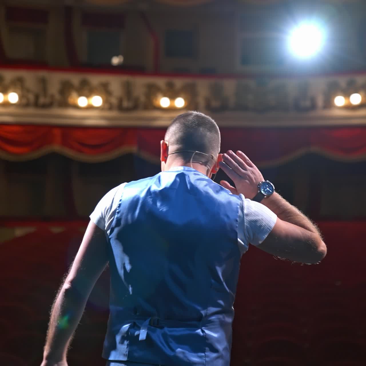 Actor rehearsing his role. Male speaker performing in front of empty auditorium in theater against bright spotlight. Back view