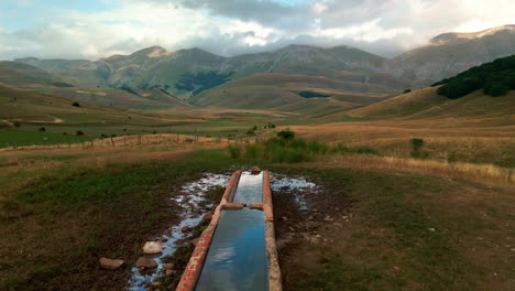 Abrevadero-Para-El-Ganado-Animal-Con-El-Valle-De-Umbría-En-La-Distancia-Durante-La-Puesta-De-Sol-Cerca-De-Castelluccio,-Italia