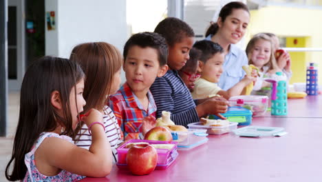 niños de la escuela primaria y el maestro en una mesa comiendo almuerzo