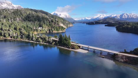 panoramic view of a serene lake with a bridge and snow-capped mountains
