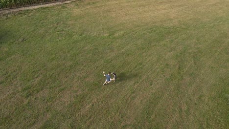 aerial top down view of a man running and playing with his dog in green field