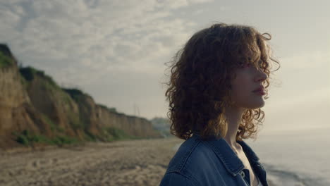 mujer rizada mirando alrededor del paisaje del océano al amanecer. niña disfrutando de la vista del mar