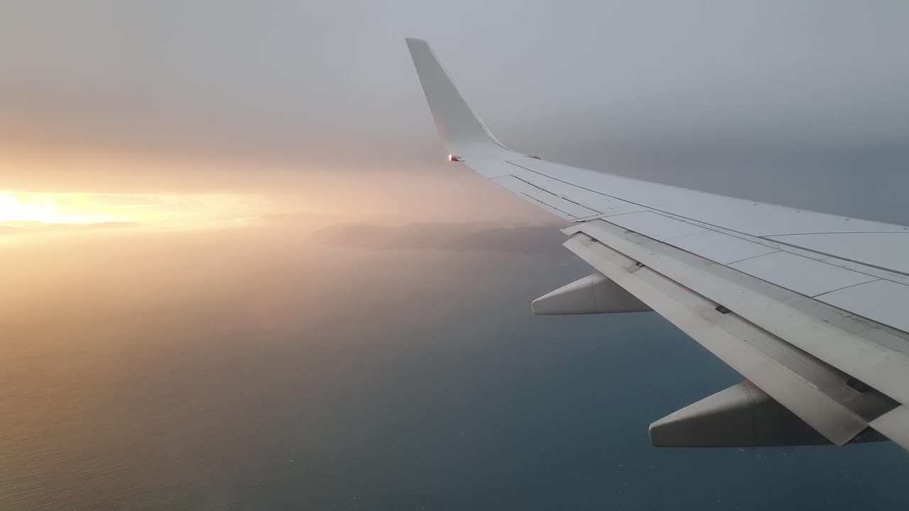 A stunning sunset seen from the airplane window looking over plane wing, land and ocean of New Zealand Aotearoa