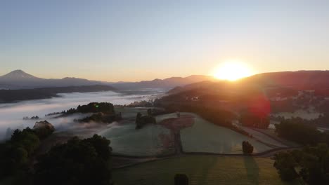 bird's eye view of a sunrise over farmland and mountains near the water's edge