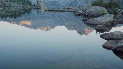 calm mountain lake with clear water reflecting peaks at sunrise in a peaceful setting