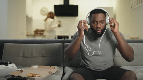 Surprised-black-man-listening-music-at-home-kitchen-with-earphones.