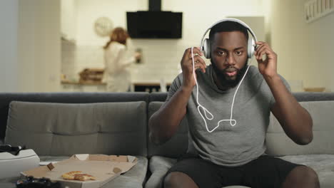 surprised black man listening music at home kitchen with earphones.