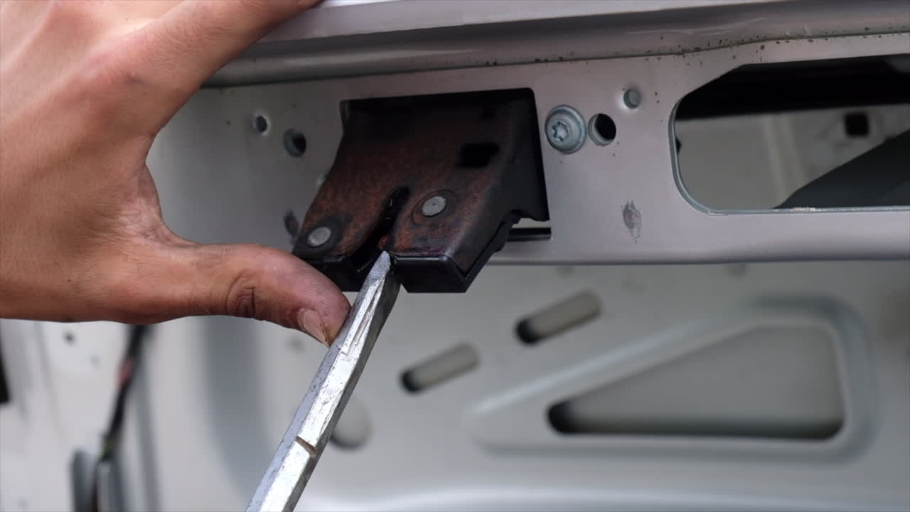 Close up of a man using a screwdriver to word on a part of the trunk of a car
