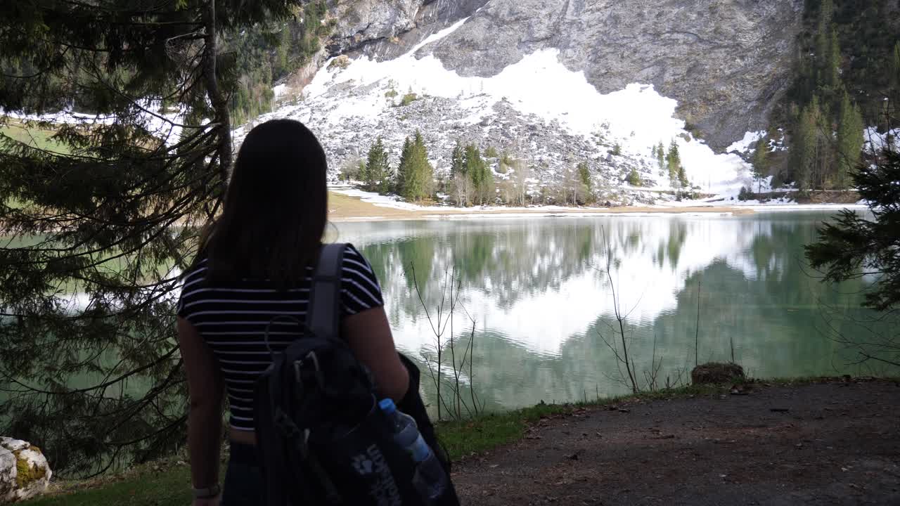 siguiente toma de una joven asiática con camisa a rayas y jeans caminando hacia un hermoso lago alp en suiza