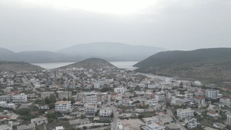 un avión no tripulado volando sobre ksamil albania por la mañana en un día gris nublado con niebla en el cielo y hoteles y casas blancas en el fondo con montañas y el registro del mar