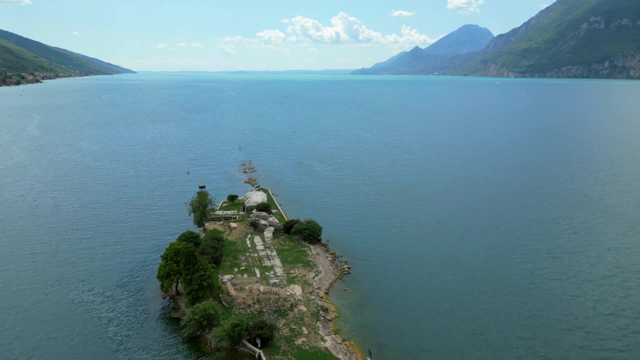 Vista aérea acercándose a las ruinas de Isola del Trimelone en el lago de Garda con un telón de fondo montañoso