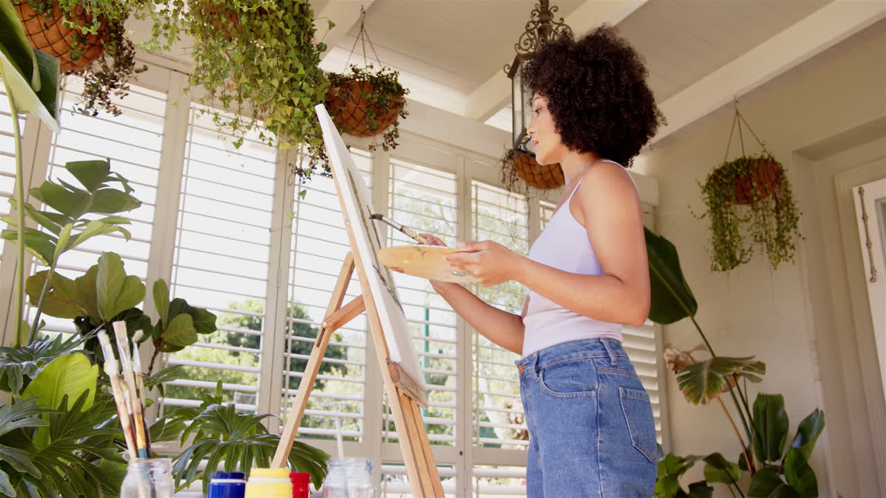 Painting on canvas, woman holding palette and brush in bright room