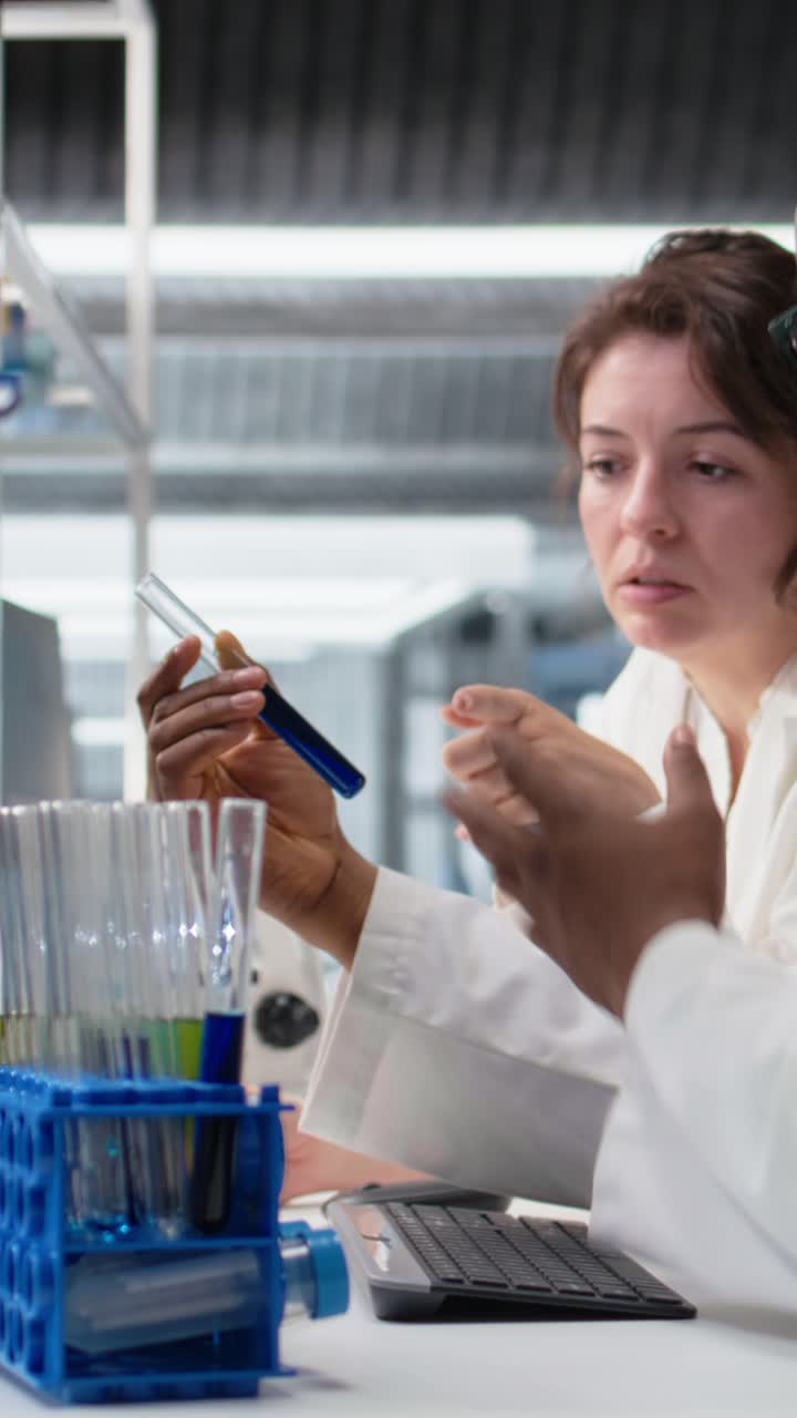 Vertical video Teamworking lab technicians inspect liquids in glass flasks