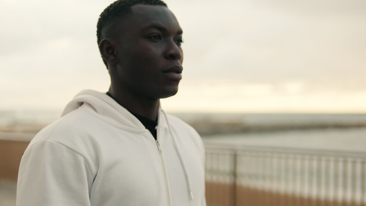 Young Black Man Standing Thoughtfully by the Ocean on a Cloudy Day