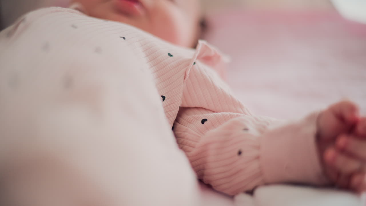 Adorable baby resting in a cozy bed under natural light, wearing pastel pink pajamas