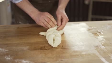 el panadero amasa la masa y hace el pan. el chef teje una coleta de la masa en la mesa. las manos del panadero de cerca. la preparación del pan. las manos masculinas de cerca