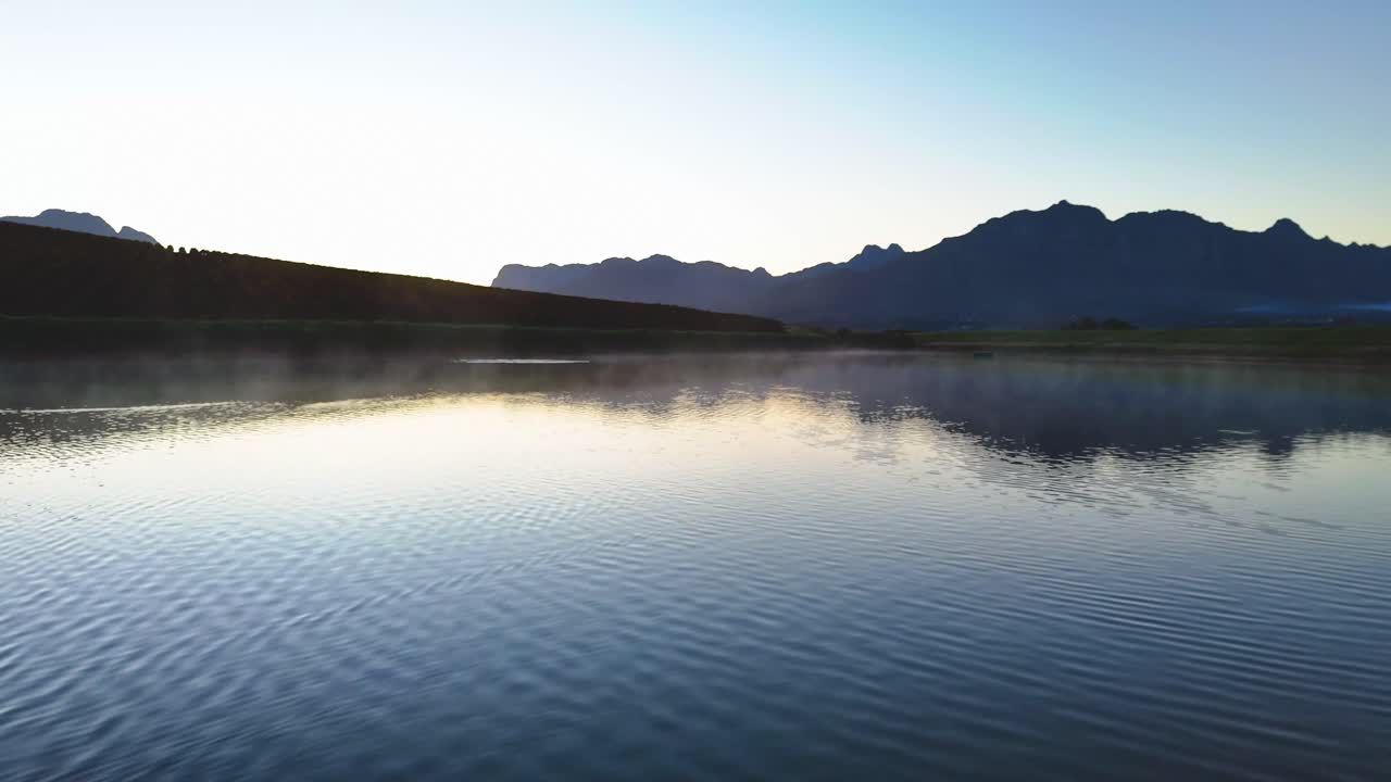 A tranquil drone hovers silently above a mirror-still lake, capturing perfect reflections of the surrounding vineyards and misty mountains in 4K