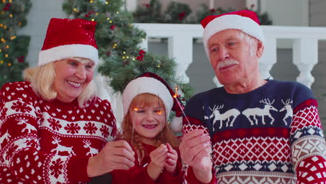 Happy-senior-couple-grandparents-with-granddaughter-holding-lit-Bengal-Christmas-lights-sparklers