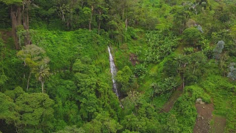 Drone-flies-towards-a-tiny-waterfall-in-the-centre-of-a-forest-covered,-mist-topped-hillside-on-a-cloudy-day