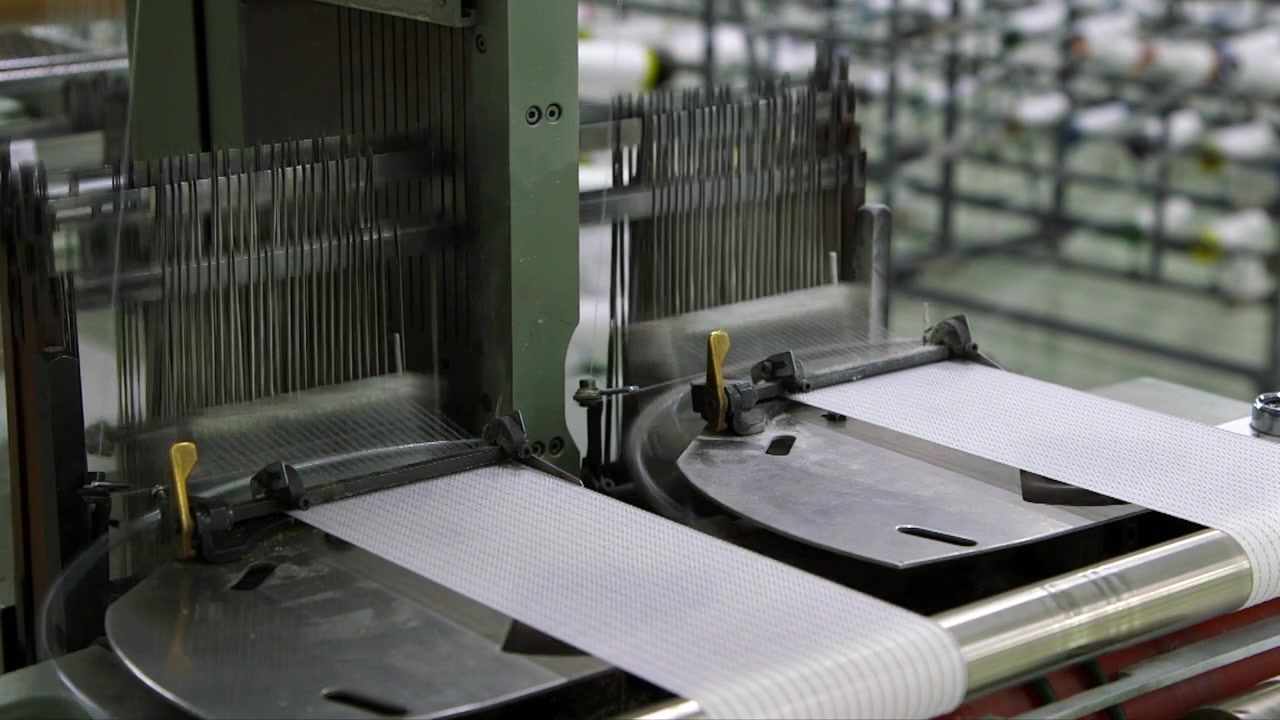 Två automatiserade industriella vävmaskiner producerar tekniskt medicinskt tyg i en modern tillverkningsanläggning. Höghastighetsproduktionsprocess för textilier för hälsovård och industriella tillämpningar.