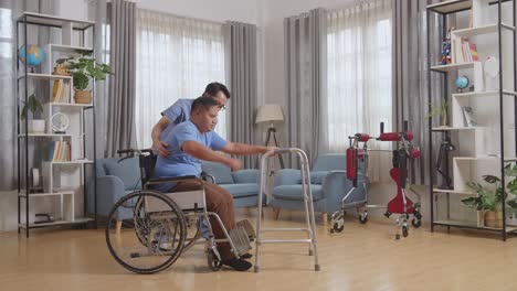 full body side view of asian male nurse helping patient in wheelchair using walker to stand by himself during a physical therapy at home