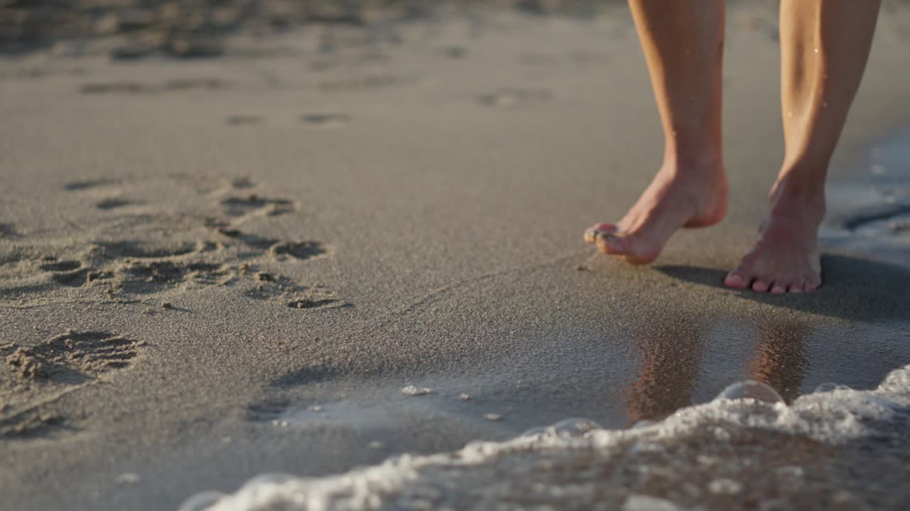 Person walking barefoot on a sandy beach with ocean waves