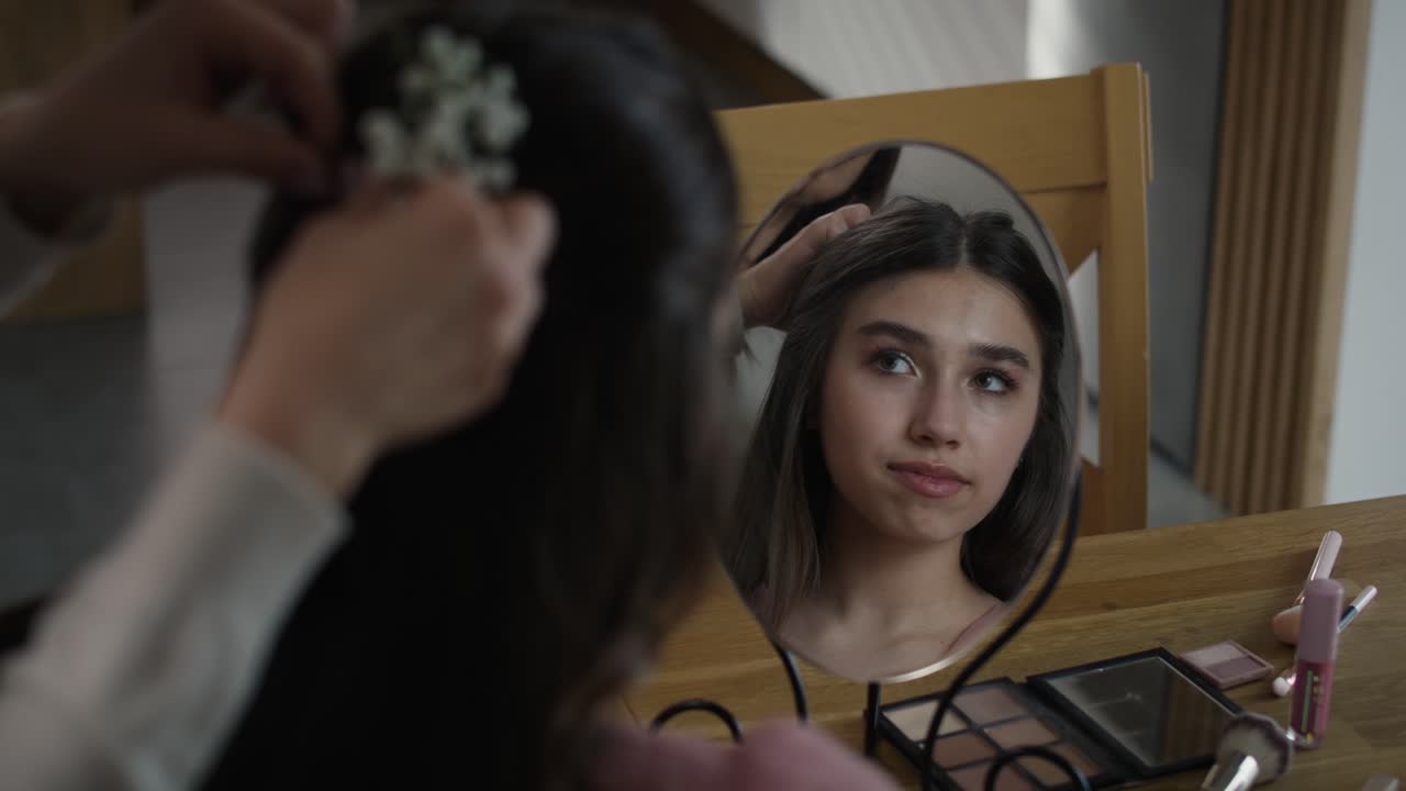 Riflesso nello specchio di una donna caucasica che acconcia i capelli a sua figlia per il ballo di fine anno