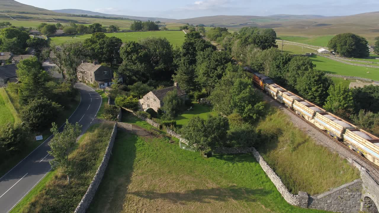 hermosa noche de verano imágenes de drones elevando y lentamente panorámica en el pueblo de selside, yorkshire, reino unido, campos, tierras de cultivo y colinas onduladas como un tren de carga pasa por debajo y en la distancia