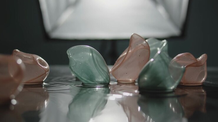 Shifting after shake, six glass petals tipping, sliding, settling on studio wet plane with softbox
